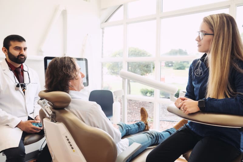 Male dentist in white coat consulting with female patient in treatment room