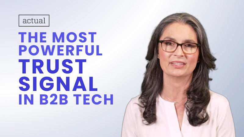 Professional woman with glasses, long wavy hair with gray streaks, and a subtle smile, wearing a light pink blouse and necklace, set against a soft blue gradient background. Overlaid text in bold blue letters reads 'THE MOST POWERFUL TRUST SIGNAL IN B2B TECH' with 'actual' in a small black-bordered box above, highlighting PR and comms as key trust builders to reduce buyer decision risk in B2B tech sales.