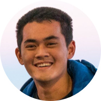 Smiling young man with short dark hair wearing a blue jacket against a light background.