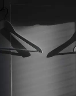 Two empty clothes hangers casting shadows on a wall with horizontal light stripes.