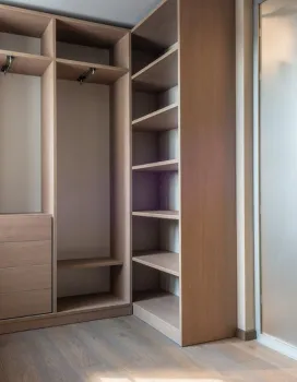 Empty wooden walk-in closet with shelves, hanging rods, and drawers next to a frosted glass door.