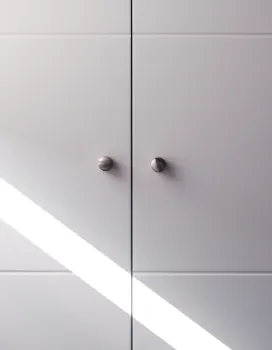 Close-up of white cabinet doors with round metal knobs and a diagonal shadow across.
