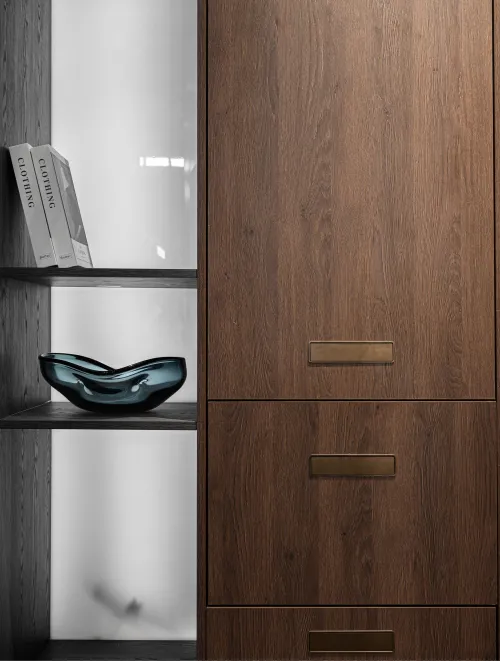 Dark wood cabinet with three brass handles adjacent to open shelves holding two books and a blue glass decorative bowl.