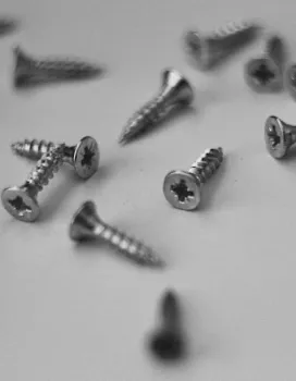 Close-up of scattered silver metal screws on a white surface.