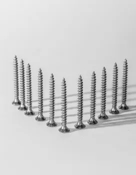Ten silver screws standing upright on a white surface, arranged in a V shape with shadows cast to the right.