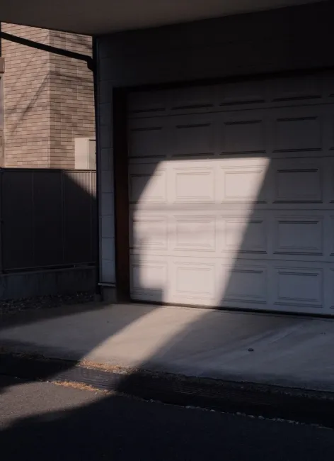 Shadow patterns cast on a closed white garage door and driveway in late afternoon light.