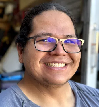 Smiling man with glasses and long hair pulled back wearing a gray shirt.