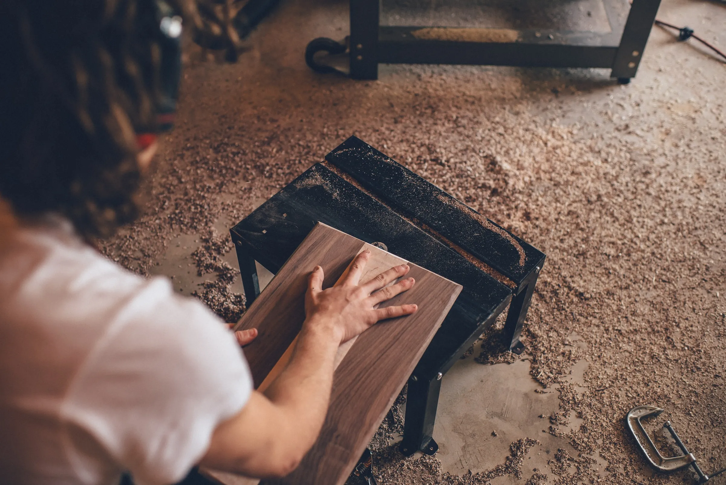 Person using a hand planer to smooth a piece of wood on a workbench covered in wood shavings.