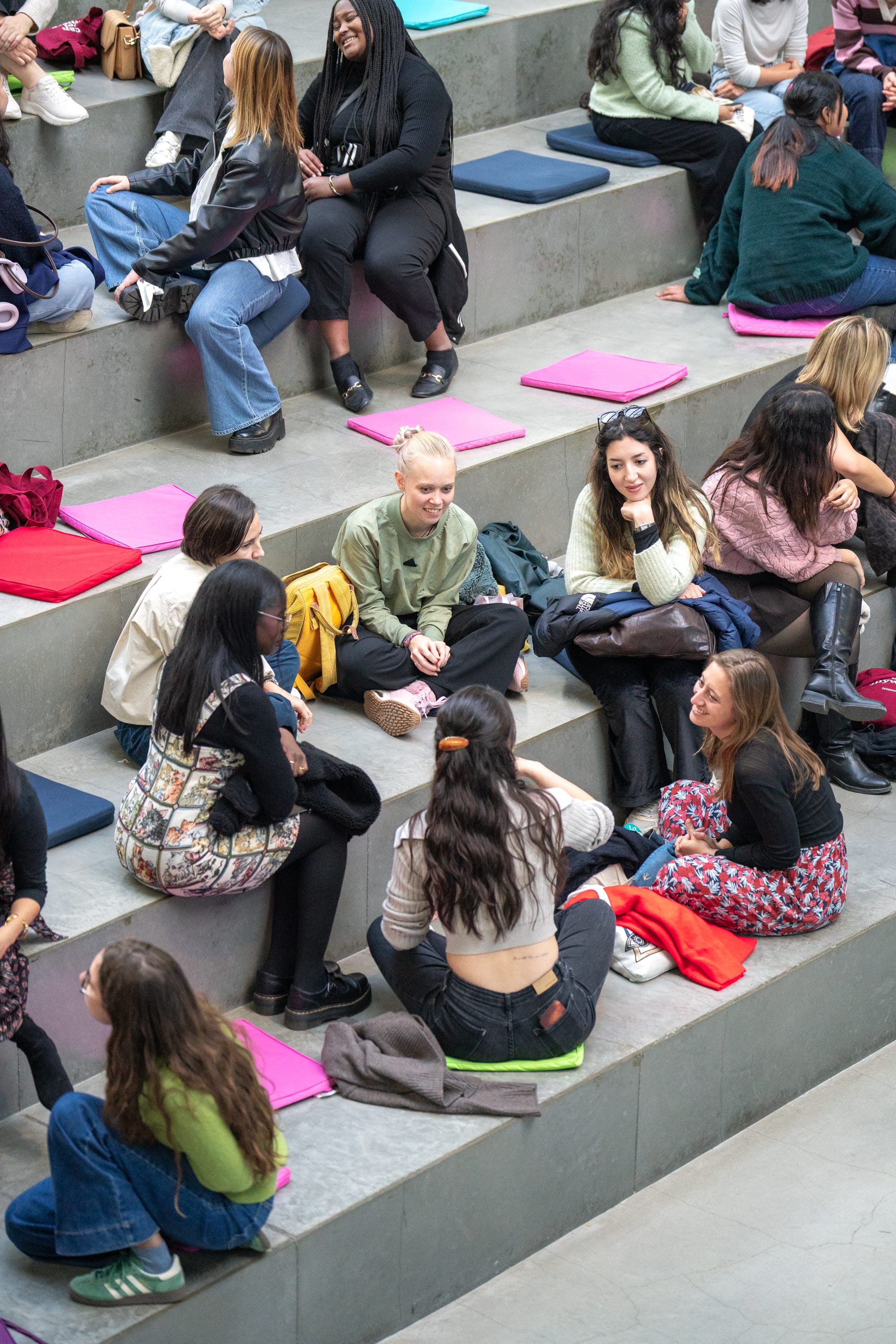 Group of young people sitting on concrete steps with colorful cushions, chatting and relaxing.