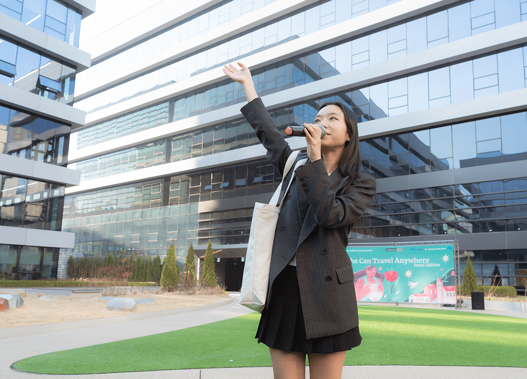 Woman waving and speaking into a microphone outside a glass building at a NomadHer event