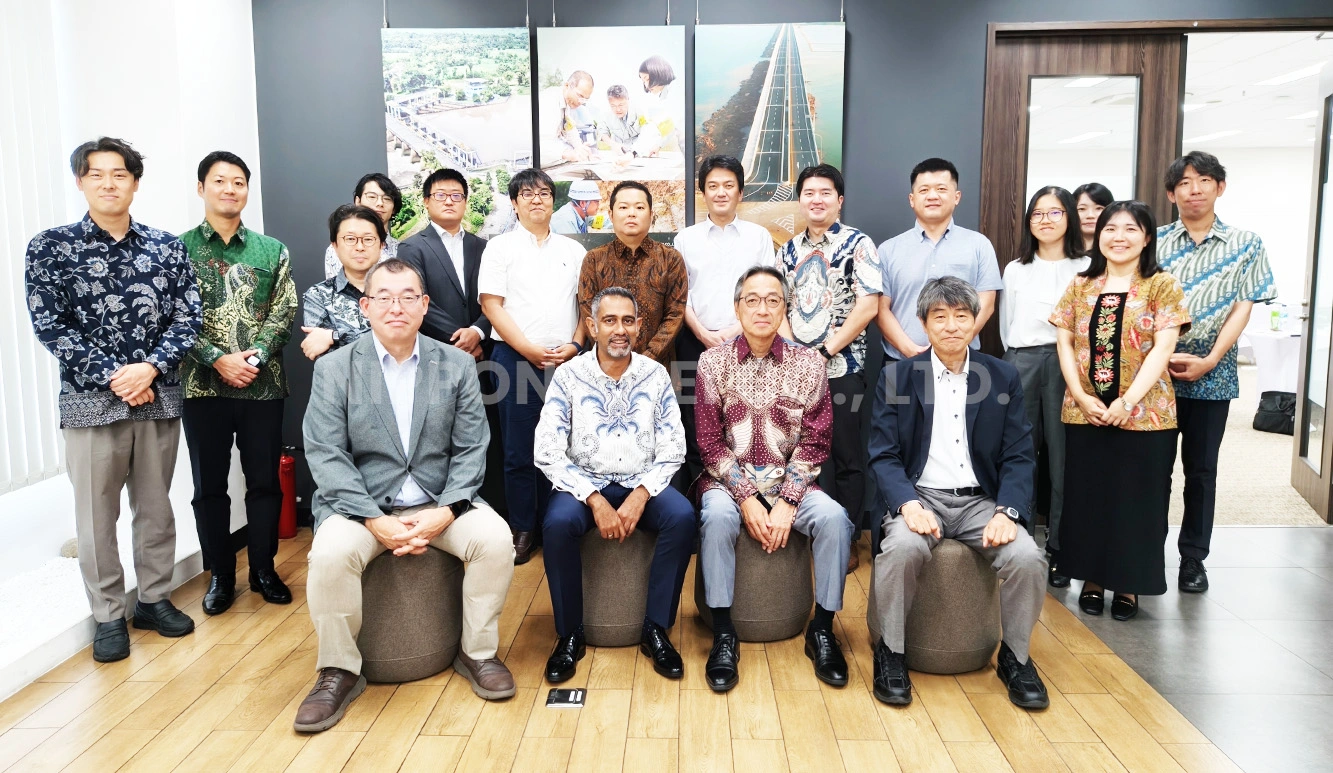 Group of 18 adults posing indoors with some seated in front and others standing behind them.