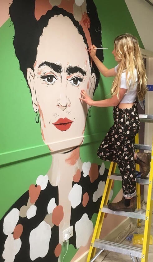 Jess painting a large mural of Freda Kahlo