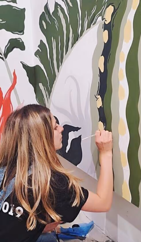 Jess painting a cactus on a wall as a mural