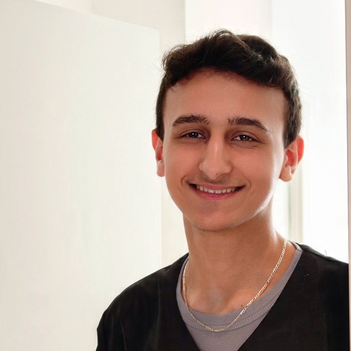 Joven sonriente con uniforme de Clínica Dental Peñota negro, camiseta gris delante de fondo blanco.