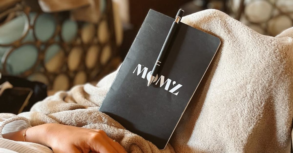 A mom'z journal and pen resting on a blanket