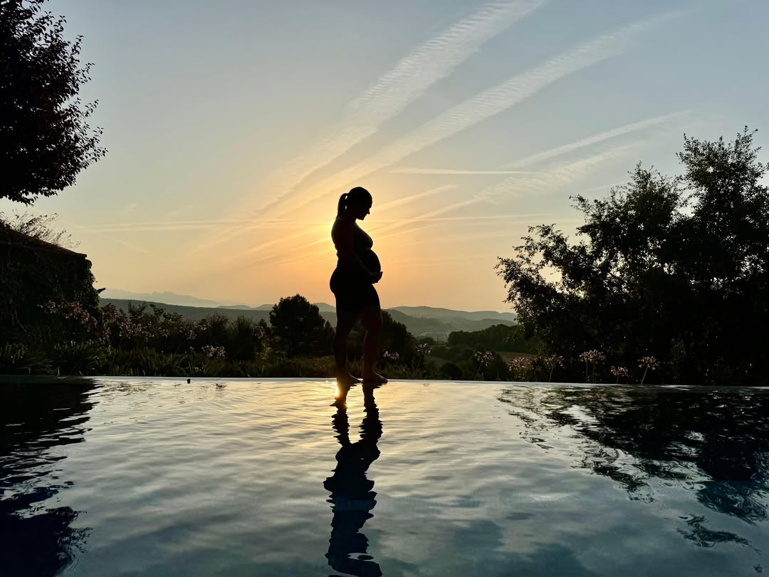 Silhouette of a pregnant woman by an infinity pool at sunset