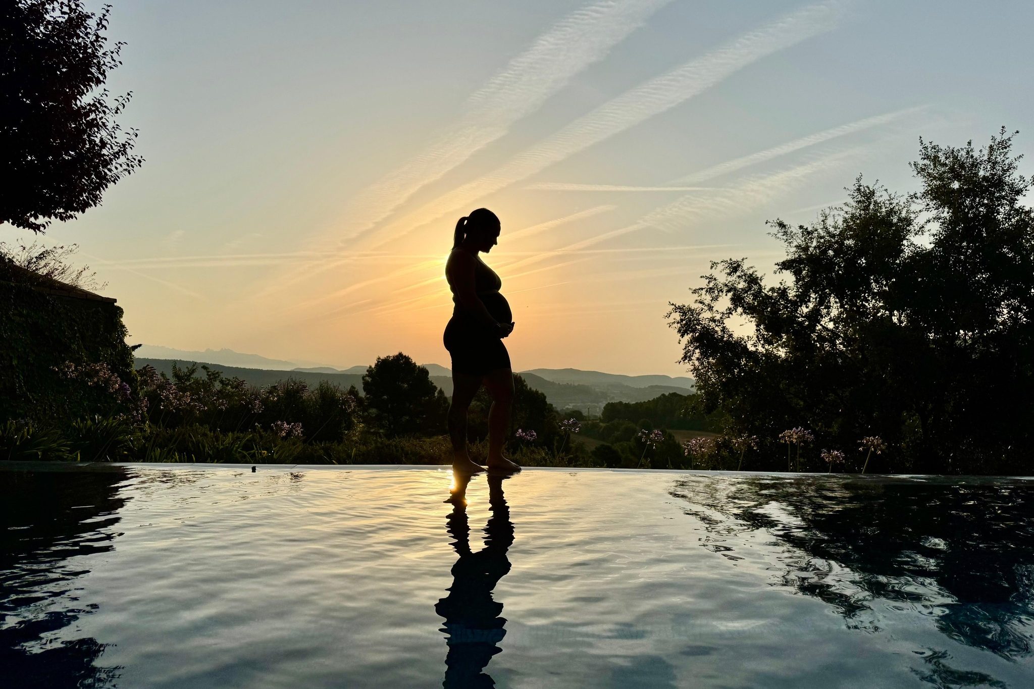 Silhouette of a pregnant woman at the infinity pool at sunset at a mom'z retreat