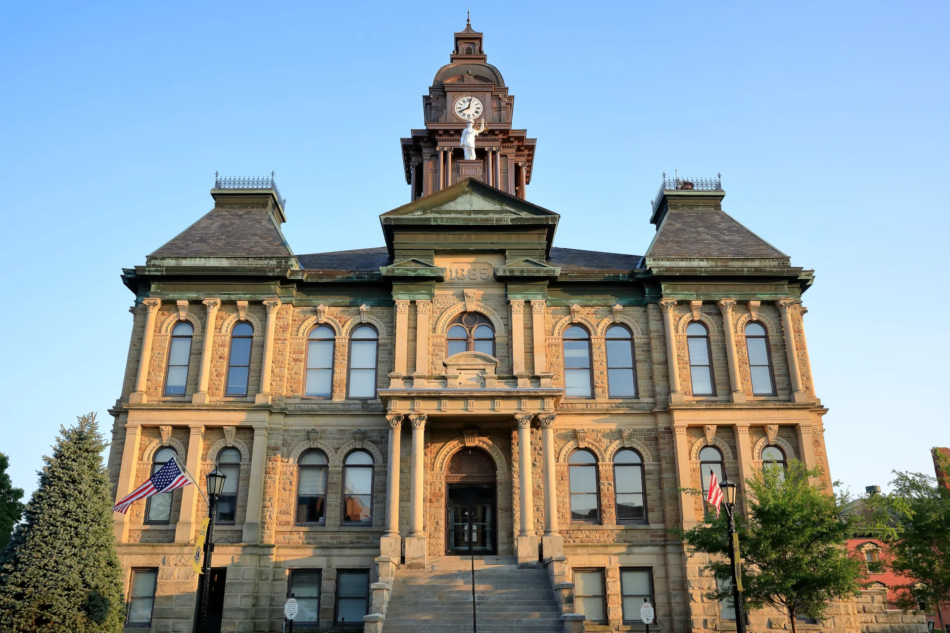 Historic stone courthouse building in Millersburg, Ohio with clock tower and American flags on either side.