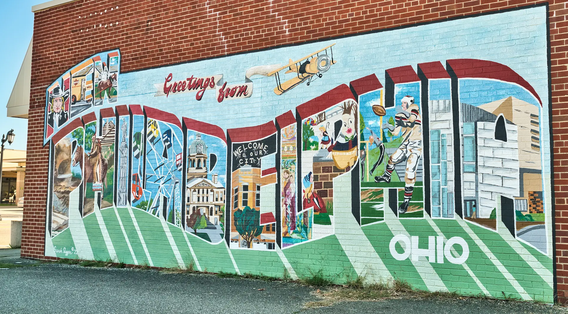 Colorful mural on a brick wall reading 'New Philadelphia Ohio' with local imagery inside each letter.