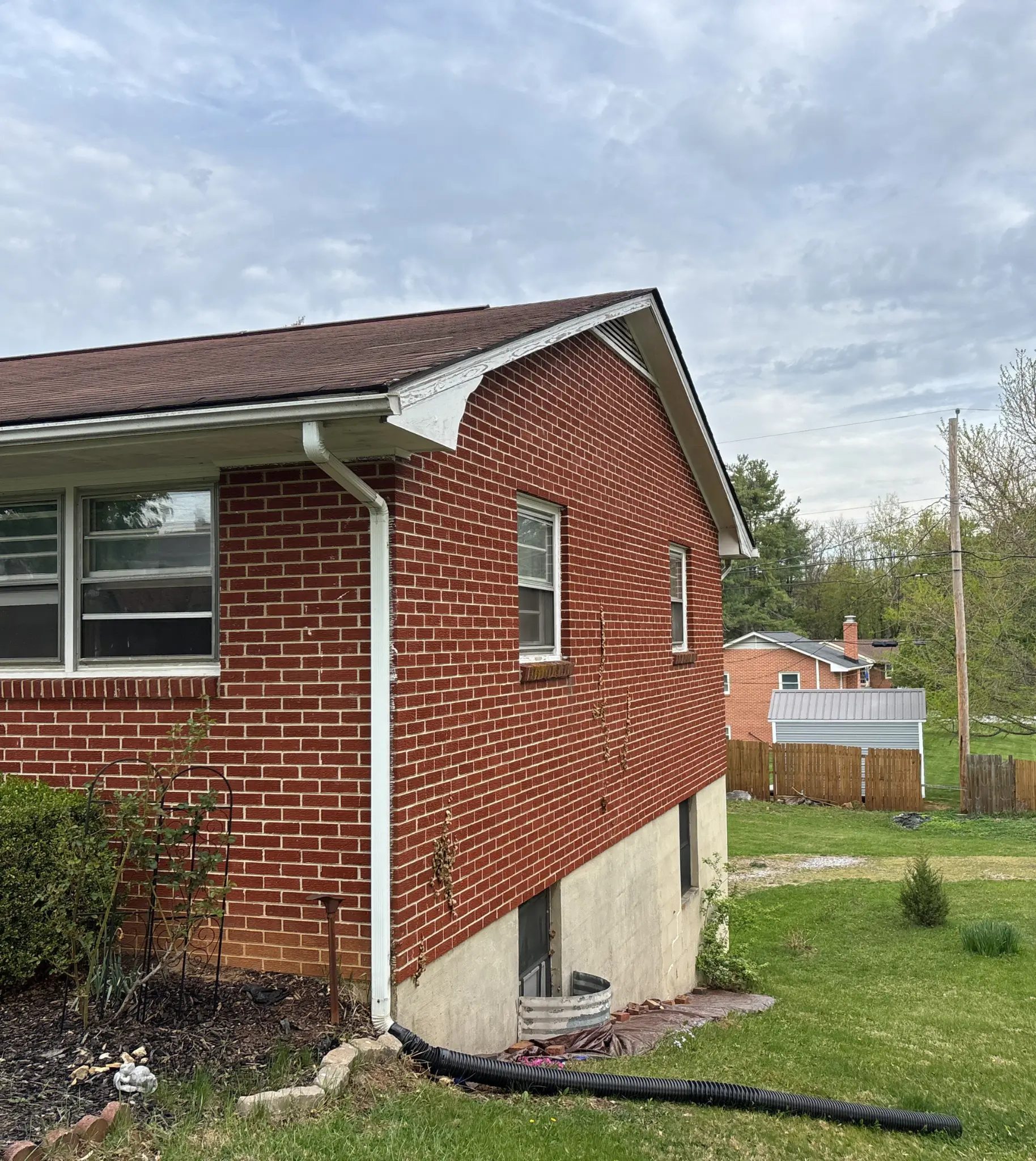 Two-story red brick home in Christiansburg, VA with a fresh Tamko Titan XT roof in Rustic Black, fronted by blooming pink phlox