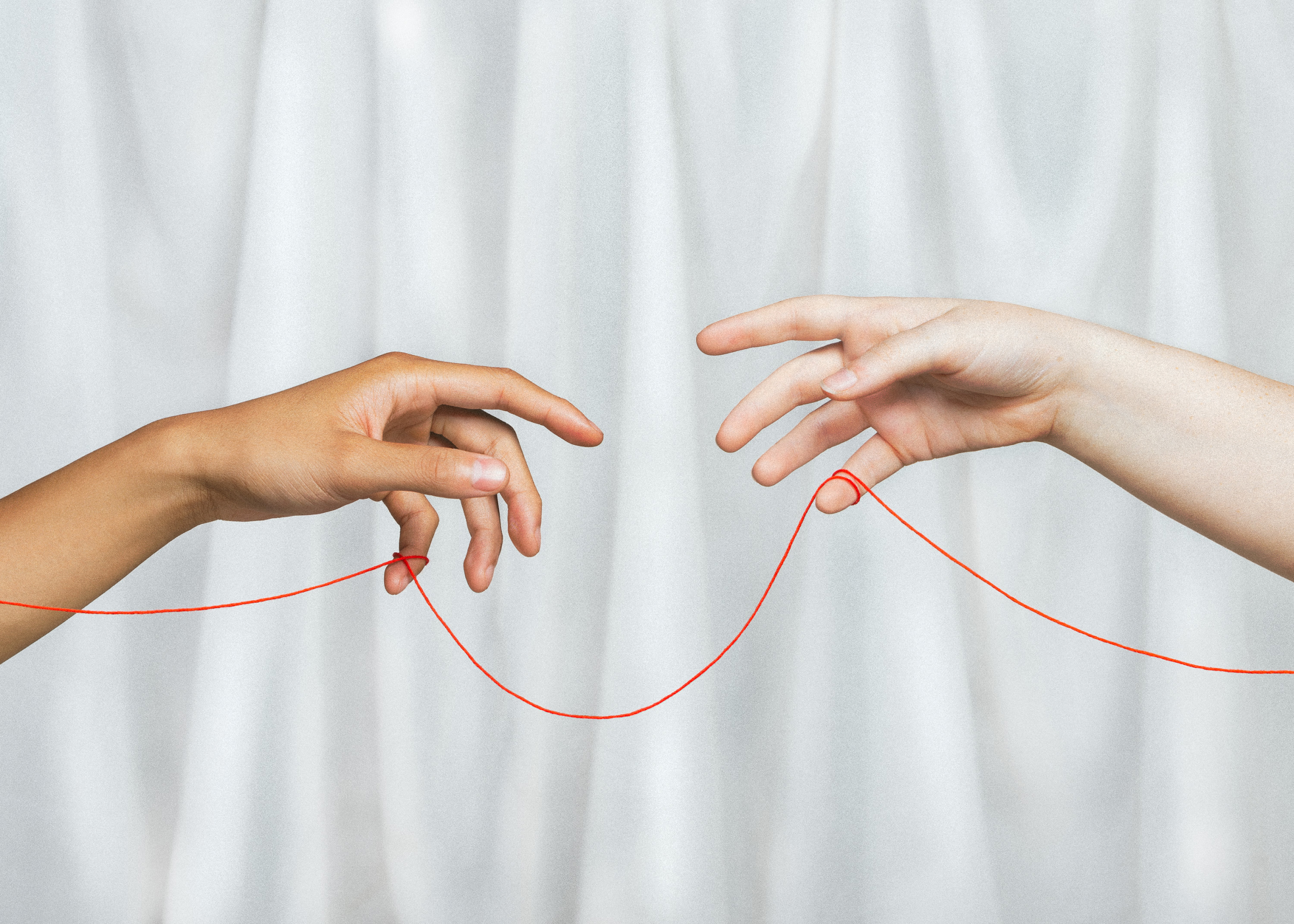 Photo of two hands with a red string connecting them, in the style of Michelangelo's famous Hand of God