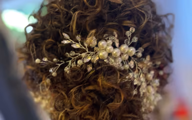 Curly brown hair styled with a decorative bridal hairpiece featuring pearls and crystals.
