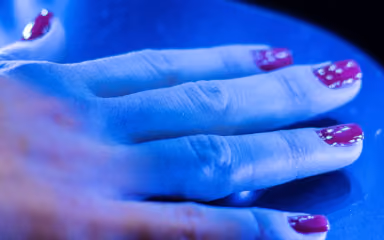 Hand with red nail polish featuring white dotted designs on fingernails under blue lighting.