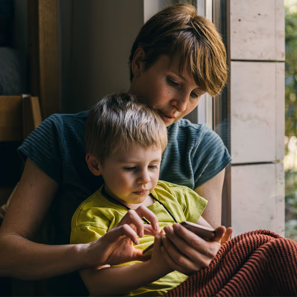 Woman and young boy sitting by window using a smartphone together.