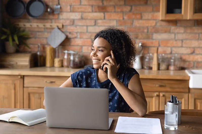 Woman smiling while on the phone and woking on a laptop