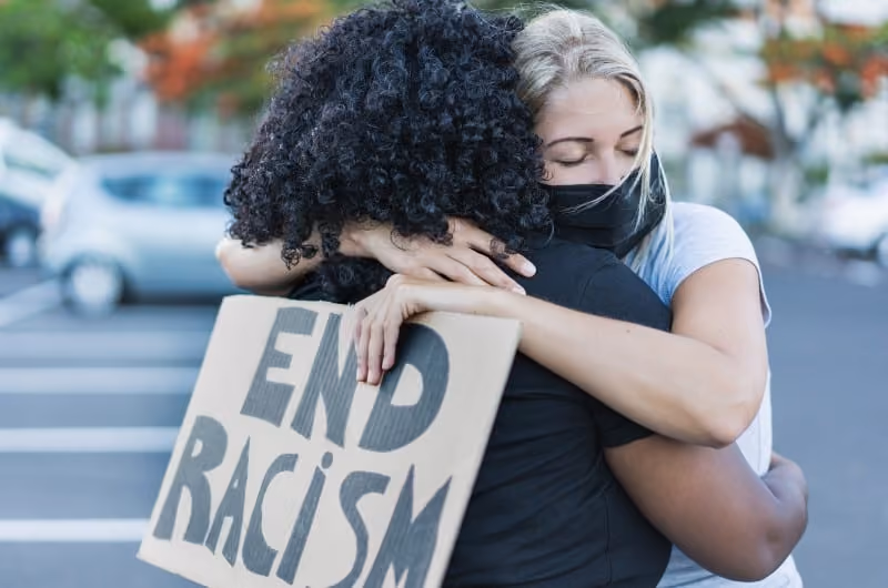 A woman wearing a facemask and holding a sign that reads End Racism,