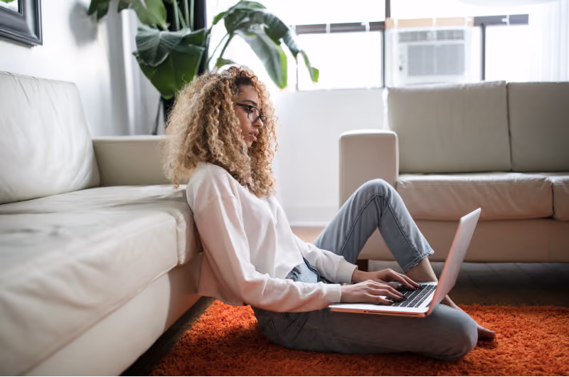 Woman in glasses sitting on the floor working on her laptop