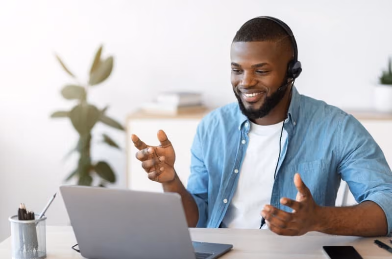 Man in an open blue shirt talking on a laptop