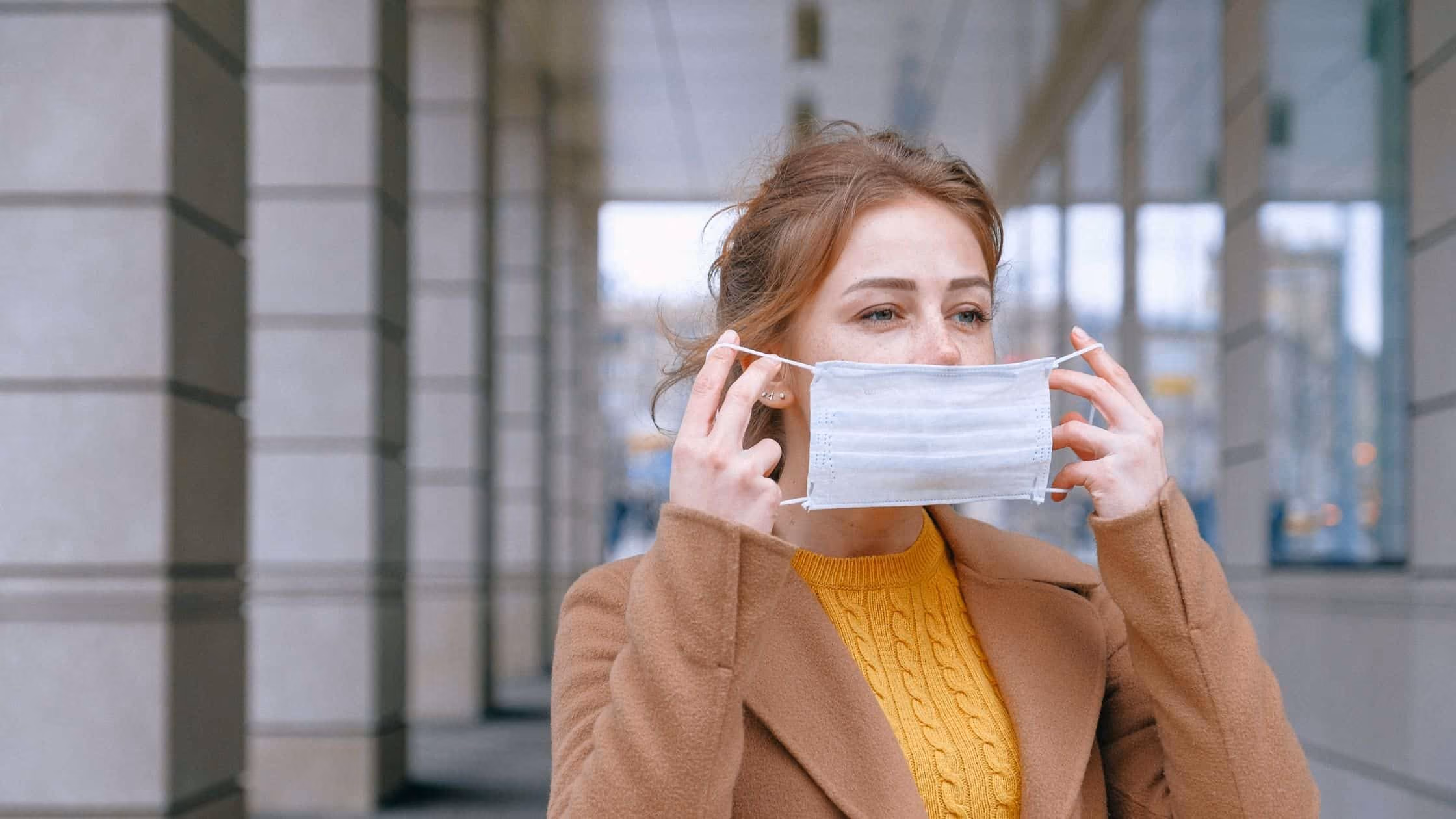 Woman in a brown cardigan putting on a facemask