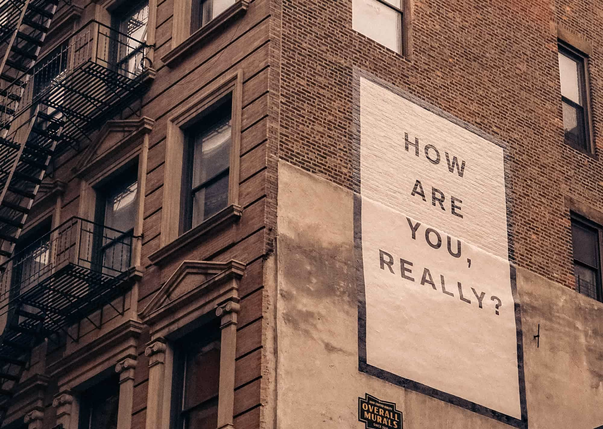A sign on a brick wall that reads How are you really doing?