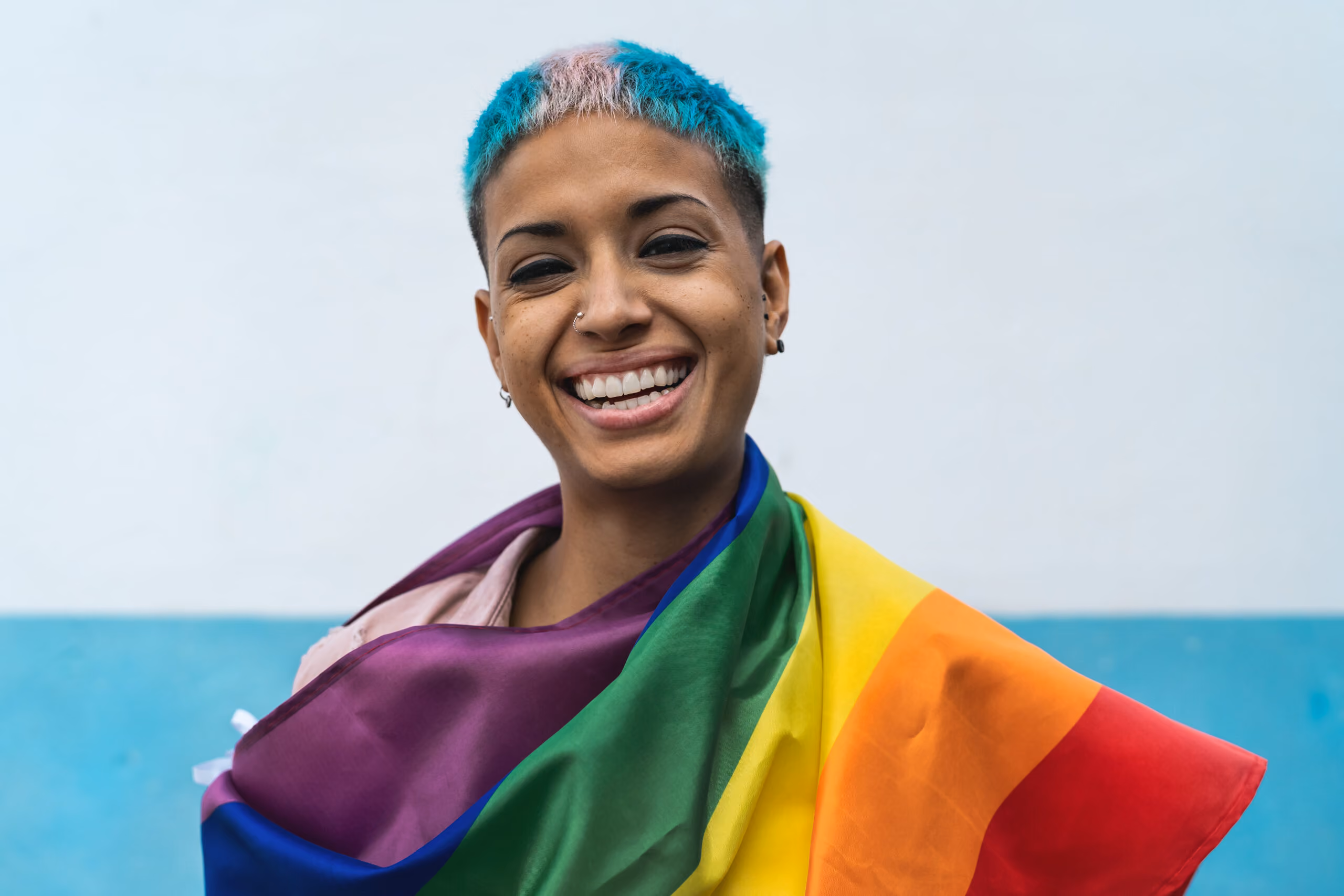 Woman with blue and pink hair draped in an LGBTQ+ flag