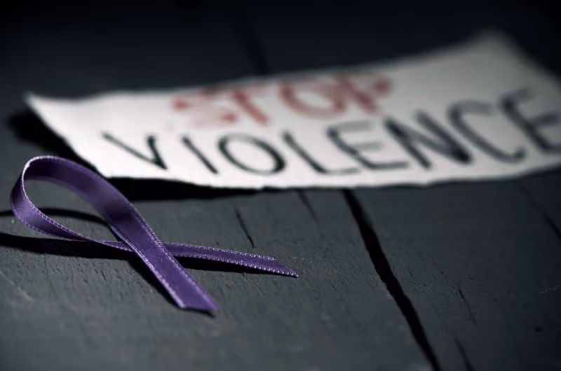 A sign on ground which reads Stop Violence next to a purple ribbon