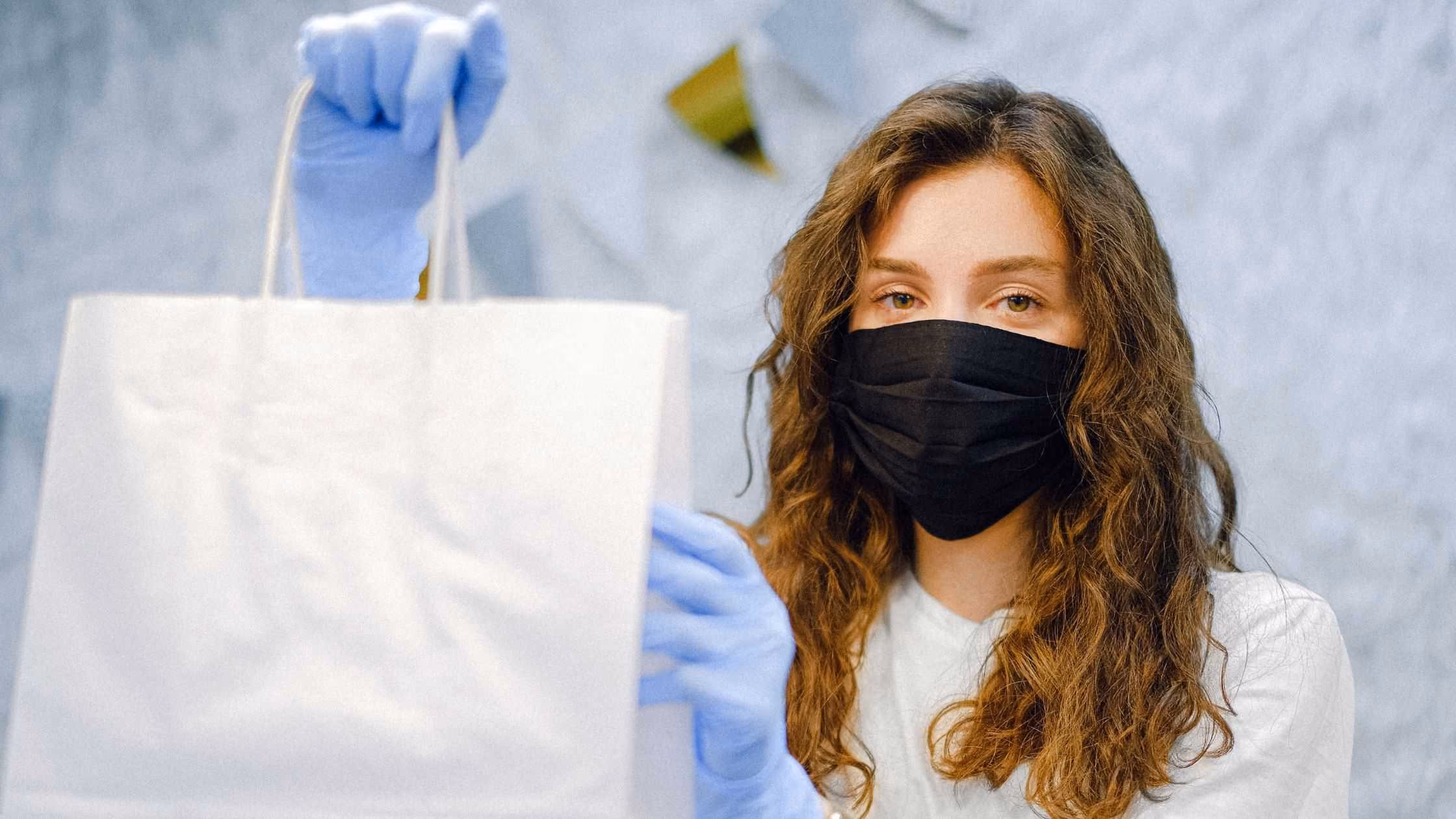 Woman in a black face mask holding up a white bag