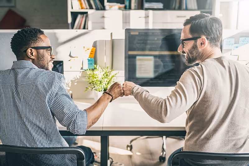 Two men in glasses fist bumping at the workplace