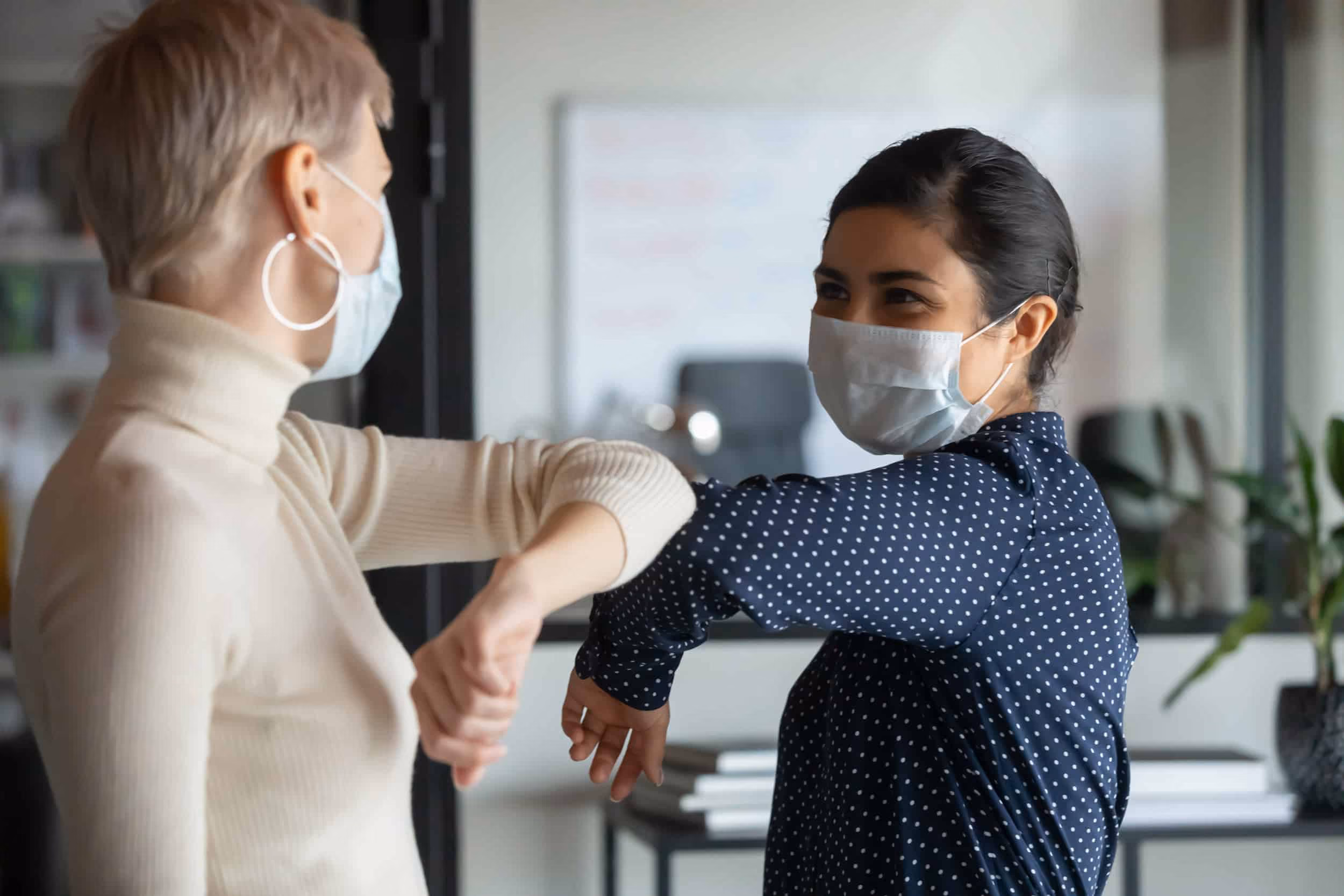 Two women in face masks tapping shoulders