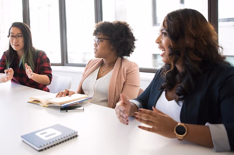 Three women sitting at a desk having a discussion