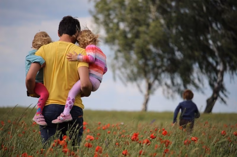 Father with his two children in his arms in a field