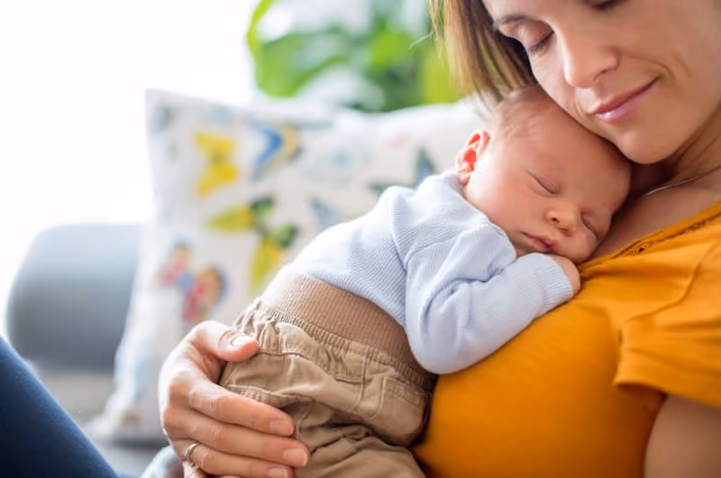 A new mother in an orange shirt holding her newborn baby