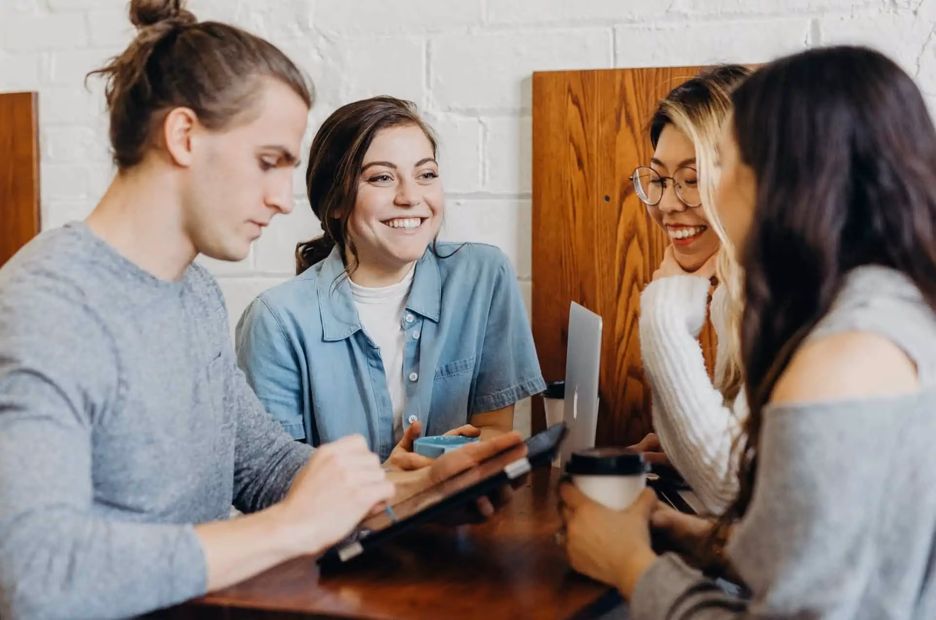 Women at work having a conversation while a man takes notes on a smart tablet