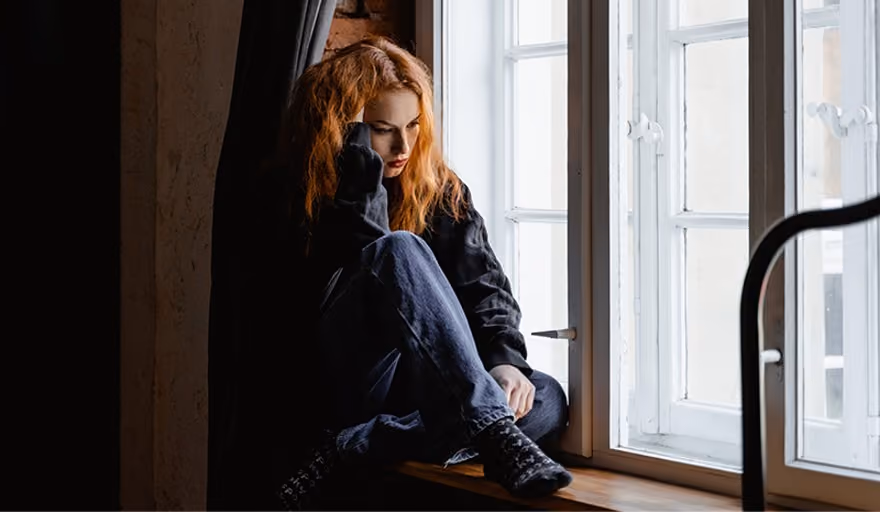 A depressed woman with substance use disorder sitting on a windowsill