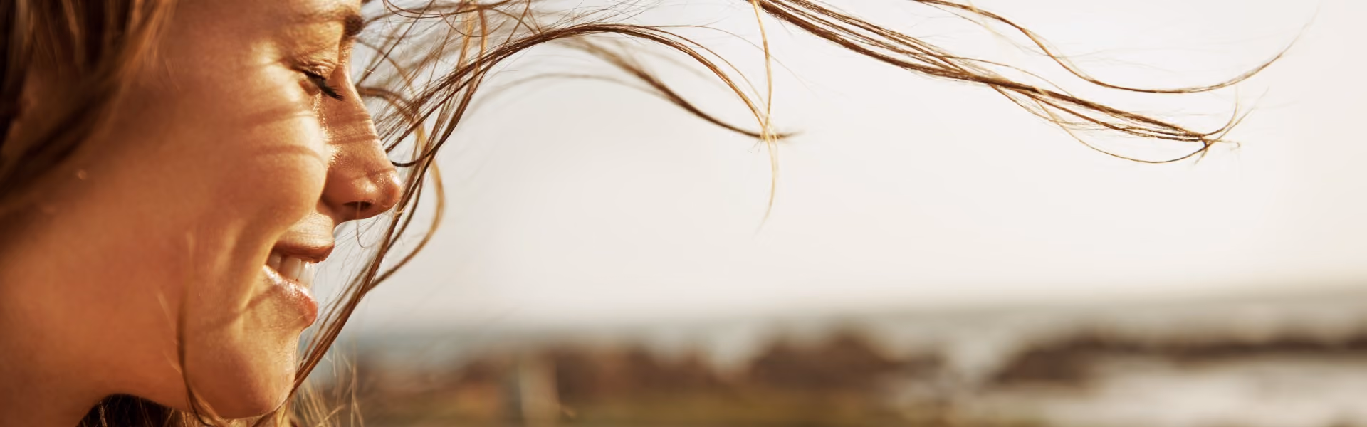 A woman smiling in a field with her hair blowing in her face
