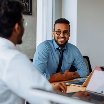 Man with glasses and a blue button down shirt talking with his colleague