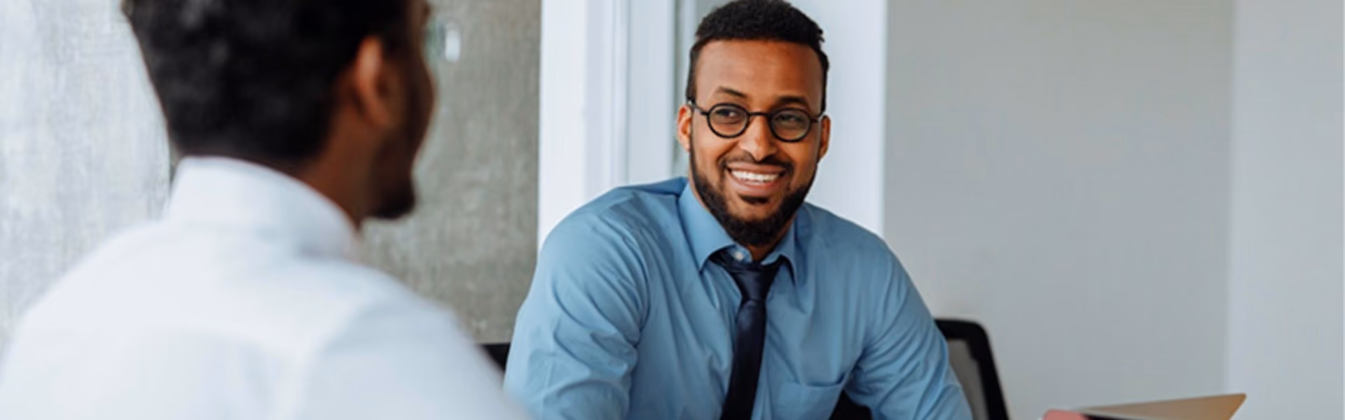 Man with glasses and a blue button down shirt talking with his colleague