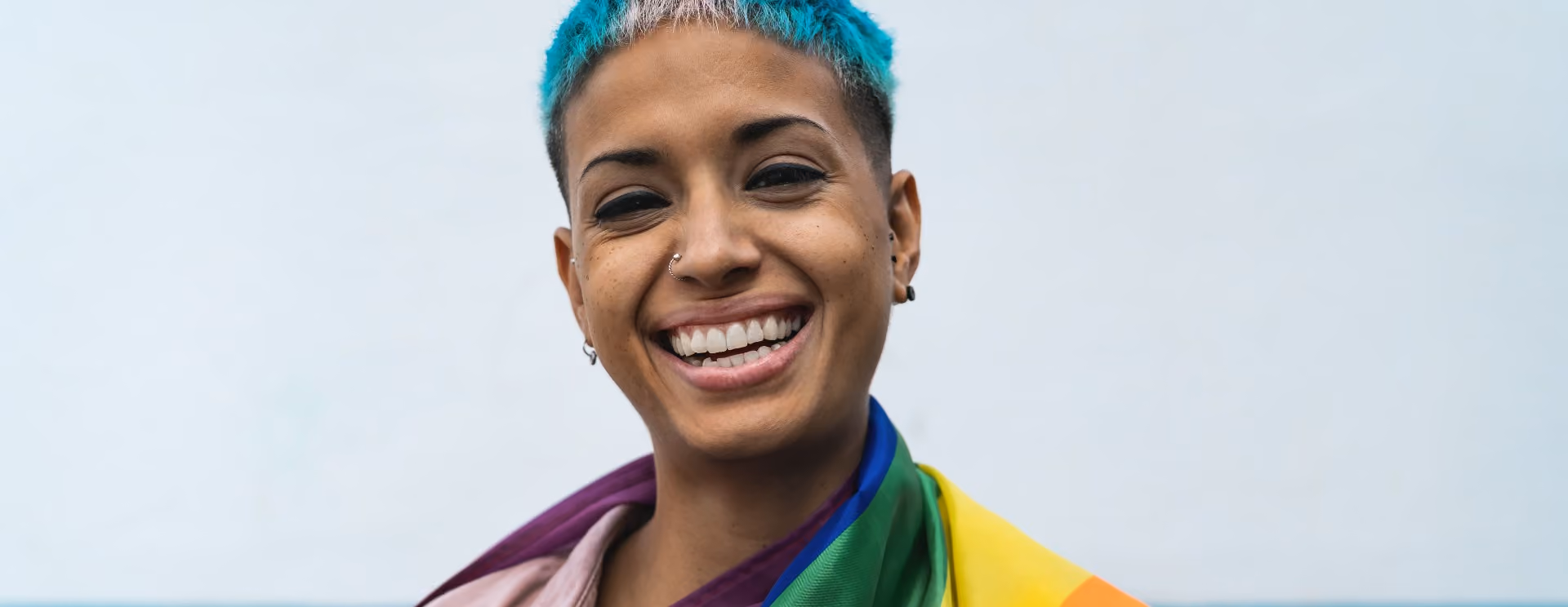 Woman with blue and pink hair draped in an LGBTQ+ flag