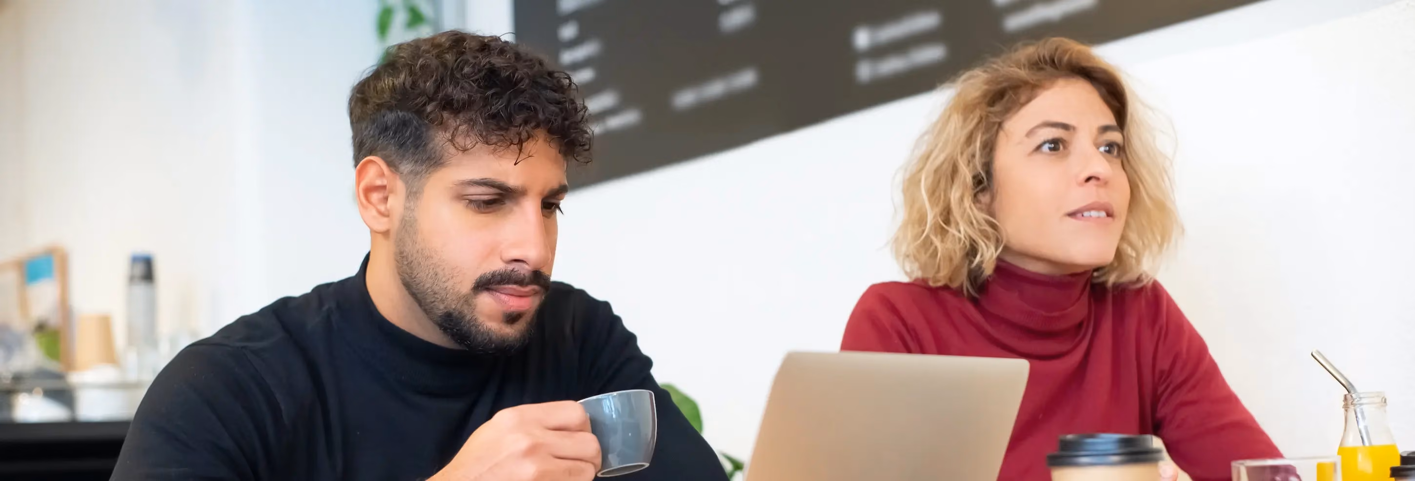 Man holding a mug drinking coffee and looking at a laptop next to a women staring outward