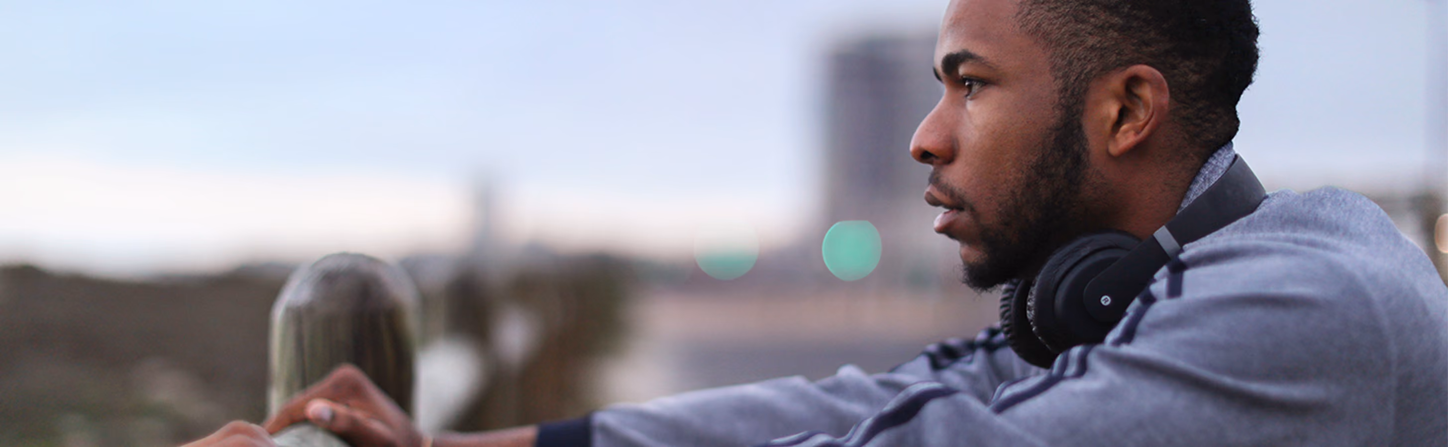 Black man with headphones around neck, stares onto a cityscape